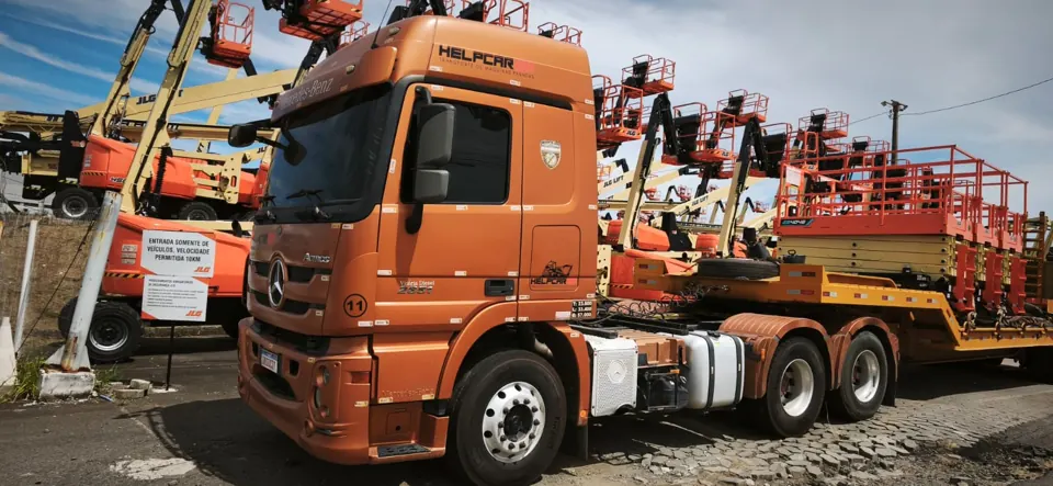Cavalo mecânico Mercedes Actros laranja da HELPCAR 101 em pátio de plataformas JLG