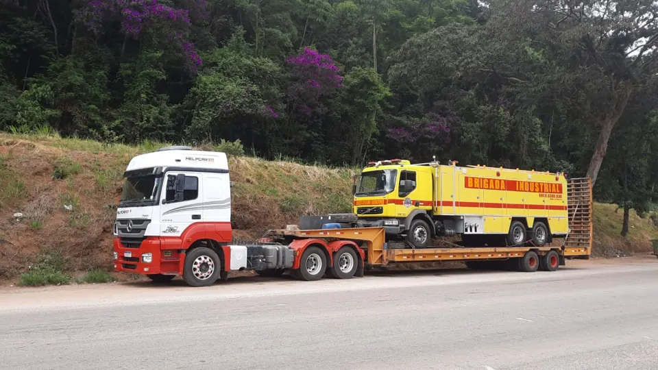 Caminhão HELPCAR 101 branco e vermelho transportando caminhão de brigada industrial em prancha