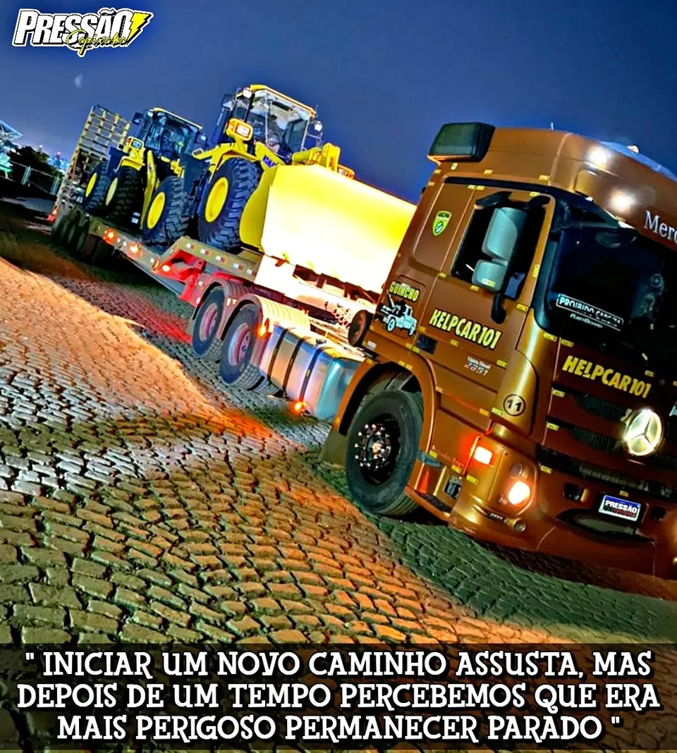 Caminhão HELPCAR 101 laranja transportando pá carregadeira em operação noturna