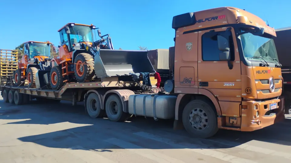 Caminhão laranja da HELPCAR 101 transportando pás carregadeiras